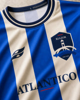 Detalle del cuello, escudo y rayas azules de la camiseta Riazor 2026