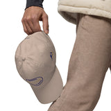 Gorra Fisterra CF Arena - detalle premium de gorra en mano con bordado lateral. Mockup oficial Printful, Costa da Morte.